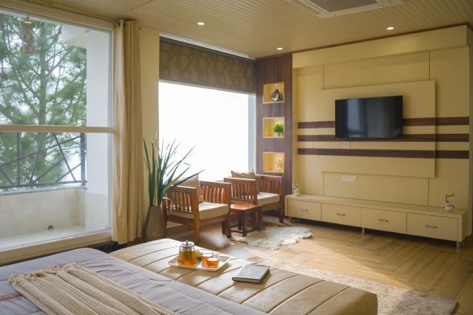 Spacious deluxe hotel room with luxury furnishings, large windows, seating area, modern lighting, flat-screen TV, and sophisticated interior design