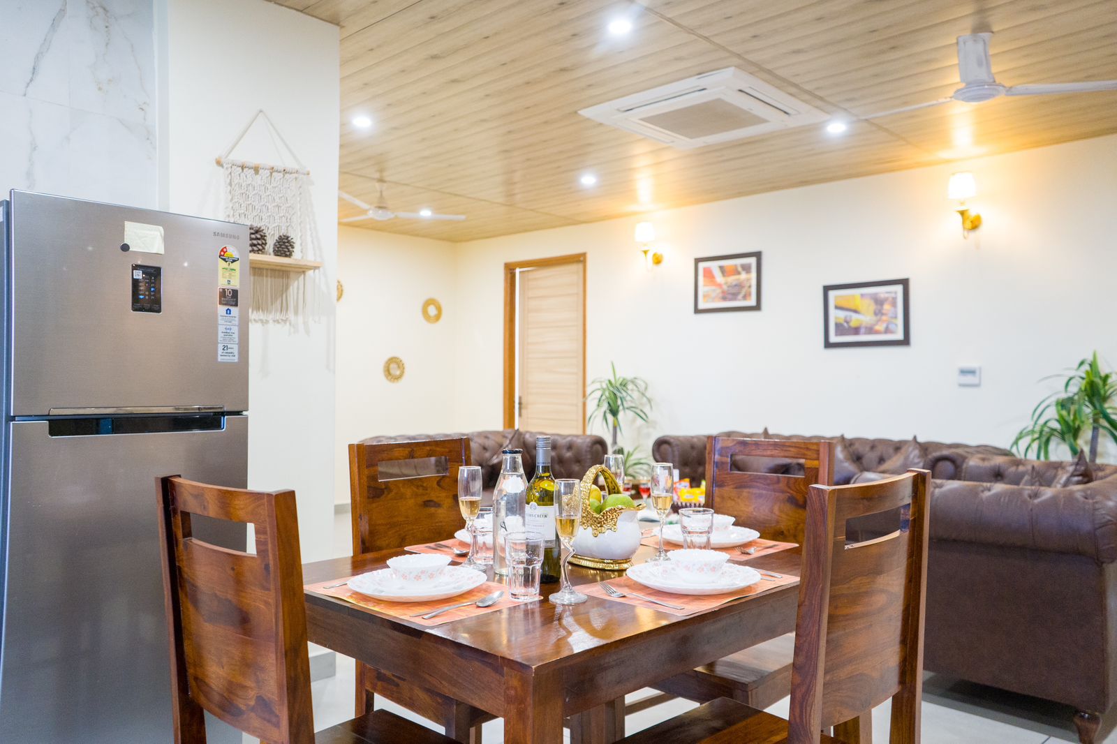 Spacious hotel dining area with wooden dining table, cushioned chairs, modern kitchen appliances, and cozy living space